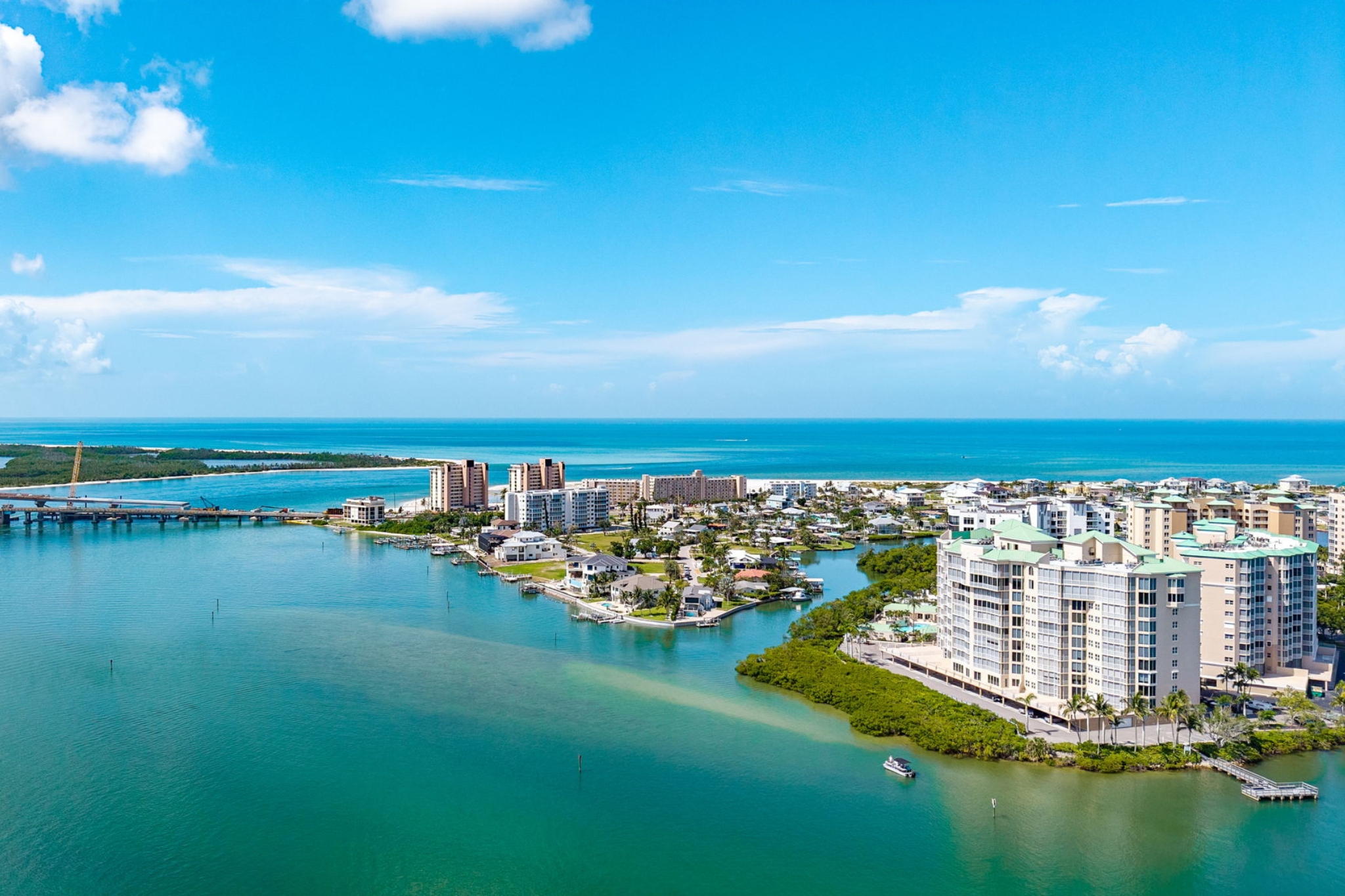 Aerial view over the Fort Myers Beach Intracoastal Waterway with waterfront homes and panoramic Gulf of Mexico horizon under blue Southwest Florida skies